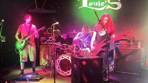A 4-piece band plays on a stage with bright green and purple lighting.